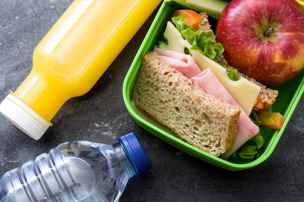 Healthy school lunch box: Sandwich, vegetables ,fruit and juice on black stone. - Photo, Image