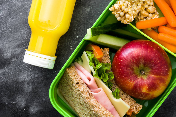 De doos van de lunch van de gezonde school: Sandwich, groenten, fruit en SAP op zwarte steen. Bovenaanzicht - Foto, afbeelding