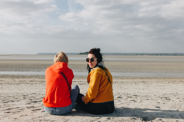 rear view of tourists sitting on sandy beach, Saint michaels mount, Normandy, France - 写真・画像