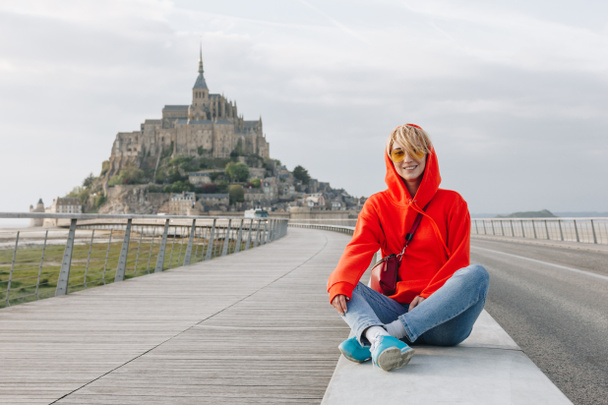 happy young woman smiling at camera while sitting near mont saint michel, france  - Photo, Image