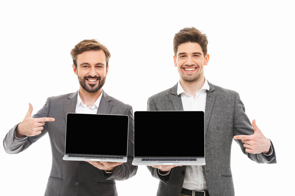 Portrait of a two happy business men pointing fingers at blank screen laptop computers isolated over white background - Fotografie, Obrázek