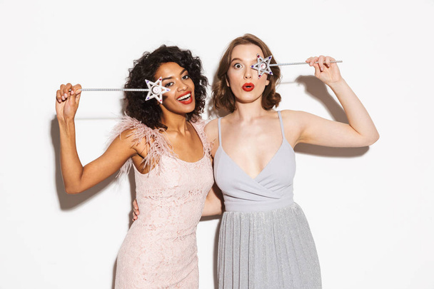 Portrait of two happy well dressed women having fun with magical wands isolated over white background - Foto, afbeelding