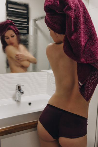 Вид сзади на сексуальную девушку в трусах и с игрушкой на голове, глядя в зеркало в ванной комнате
 - Фото, изображение
