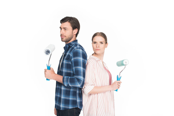  young couple with paint rollers standing back to back isolated on white background  - Φωτογραφία, εικόνα