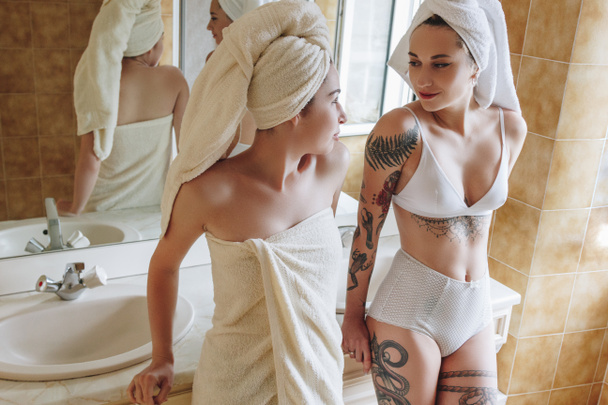 beautiful girlfriends in underwear and towels looking at each other in bathroom - Photo, Image