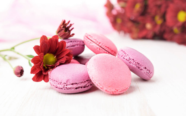 Set of french macaroons on wooden table. Sweet pink and violet macaron cakes and a red chrysanthemum flowers. - Photo, Image