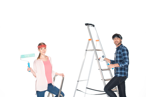vriend en vriendin op ladders met verf rollers geïsoleerd op witte achtergrond  - Foto, afbeelding