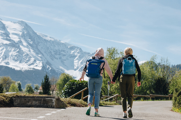 back view of girls with backpacks holding hands and walking on mountain road, mont blanc, alps - Фото, изображение