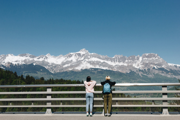back view of girls standing near fence and looking at majestic snow-capped mountains, mont blanc, alps - Photo, Image