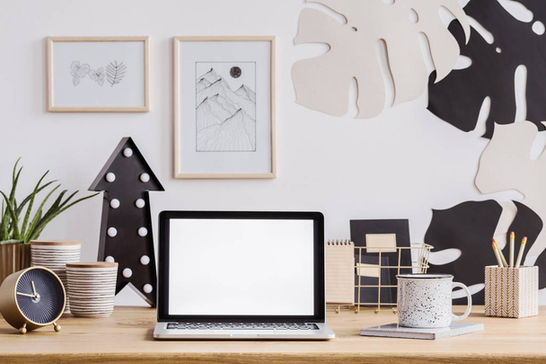 Laptop-val fehér képernyő, egy fából készült íróasztal, óra, korsó és ceruza, valamint fali dekorációk - Fotó, kép