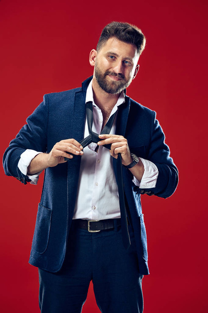 Businessman tying his tie at red studio - Fotografie, Obrázek