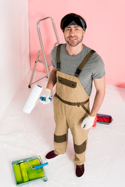 high angle view of man in protective gloves and working overall holding paint roller  - Photo, Image