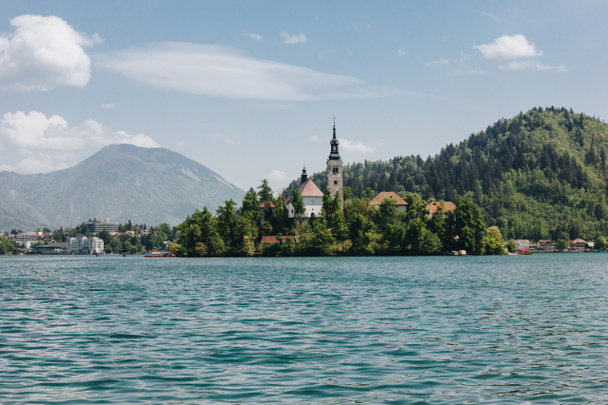 old architecture and green trees at bank on scenic mountain lake, bled, slovenia - Zdjęcie, obraz