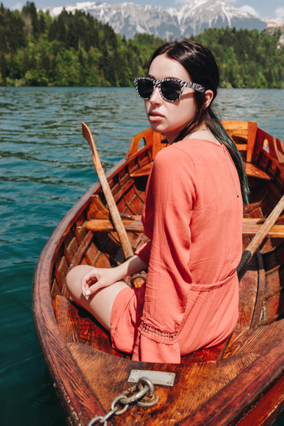 hermosa mujer joven en gafas de sol sentado en barco en el tranquilo lago de montaña, sangró, slovenia
 - Foto, Imagen