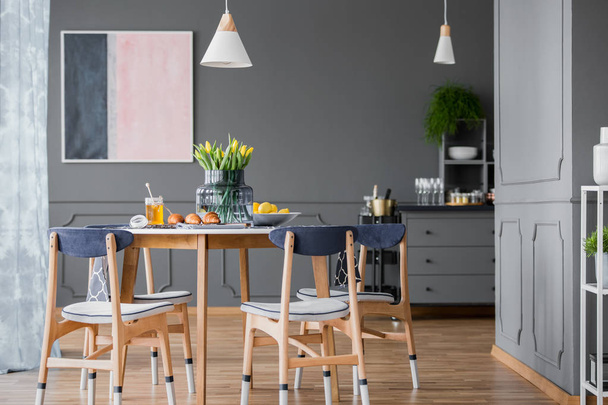 Grey dining room interior with pink and blue painting, wooden table and chest of drawers - Foto, Bild