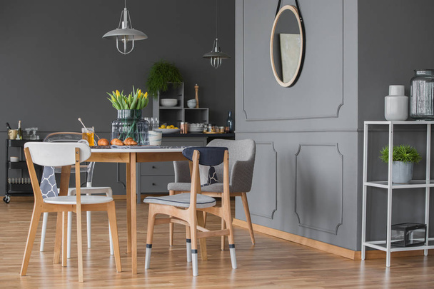 Vista lateral do interior da cozinha cinza com uma mesa de jantar, cadeiras, espelho e moldagem de parede
 - Foto, Imagem