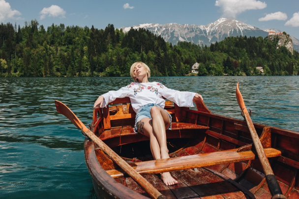 スロベニアのブレッド、静かな山の湖でボートで休んでいる美しい若い女性 - 写真・画像