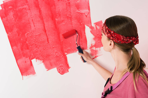 back view of woman in headband painting wall in red by paint roller  - Фото, изображение