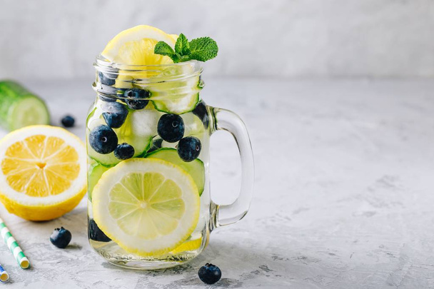 Infused detox water with lemon and cucumber slices, blueberry and mint. Ice cold summer cocktail or lemonade in glass mason jar - Photo, Image