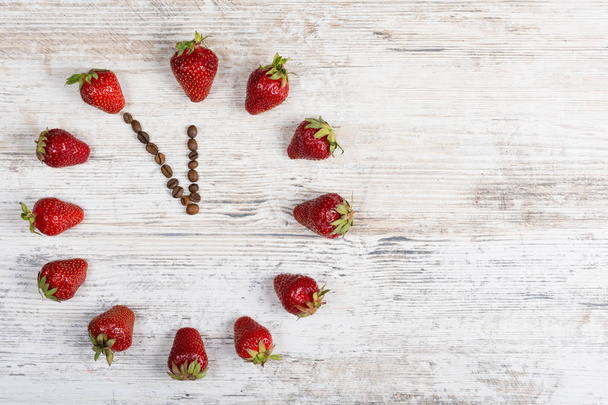 Erdbeeruhr mit Pfeilen aus Kaffeebohnen, die die Zeit von elf Stunden fünfundzwanzig Minuten oder dreiundzwanzig Stunden fünfundfünfzig Minuten auf einem Holztisch in der Küche anzeigt - Foto, Bild