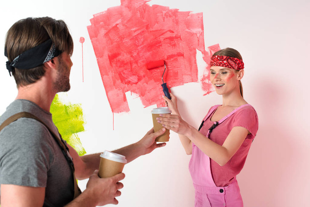 Nuori mies antaa paperin kuppi kahvia hymyilevä tyttöystävä, kun hän maalaus seinään
  - Valokuva, kuva