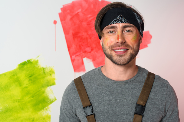 portrait of smiling man with painted face in headband standing in front of painted wall - Photo, image