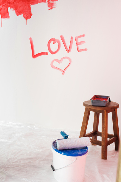 wall with lettering love and heart symbol, paint tin with paint roller and chair with roller tray  - Photo, Image