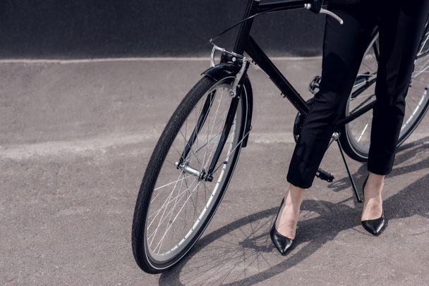 recortado disparo de mujer de negocios en traje y tacones altos de pie cerca de bicicleta retro en la calle
 - Foto, Imagen
