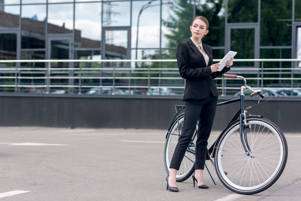 young businesswoman with digital tablet standing near retro bicycle on street - Foto, afbeelding