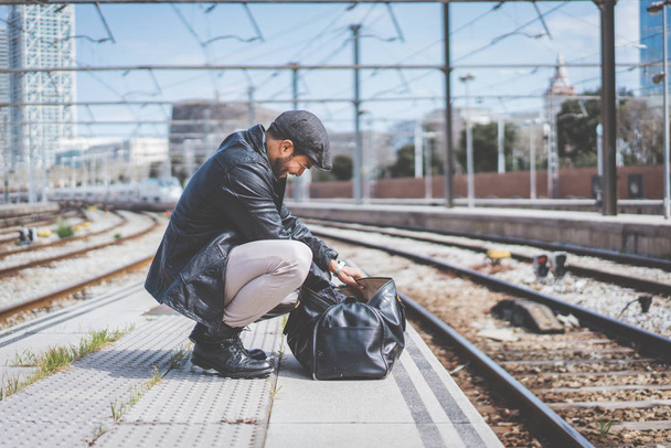 Attractive confident hispanic man having a backpack front of him with a clothes bag, walking beside a platform at train station. - Foto, Imagem