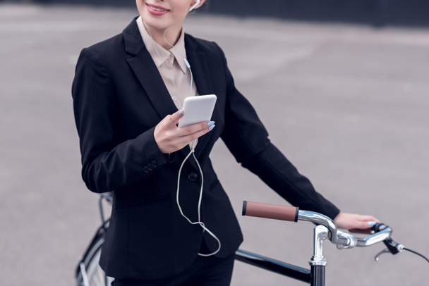 levágott lövés üzletasszony-fülhallgató-val smartphone áll közel utcán retro kerékpár - Fotó, kép