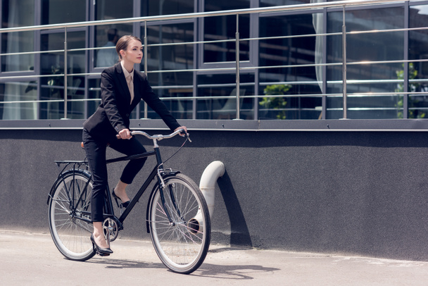 side view of young stylish businesswoman in suit riding retro bicycle - Photo, Image