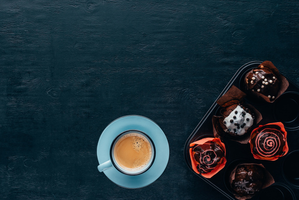 Vista superior de deliciosas magdalenas con esmalte y taza de café azul sobre fondo de madera
 - Foto, Imagen