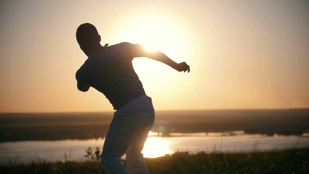 Ottelija suorittaa capoeira temppuja kukkulalla kesällä auringonlasku, hidastettuna
 - Materiaali, video