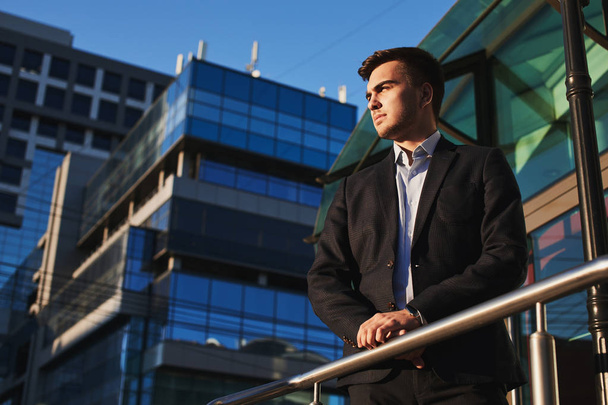 confident businessman leaning on railing while standing on porch of building in city center   - Foto, Imagen