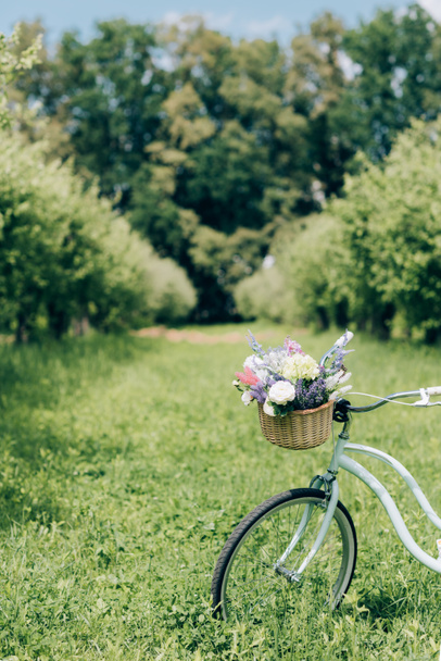 selective focus of retro bicycle with wicker basket full of flowers at countryside - Fotó, kép