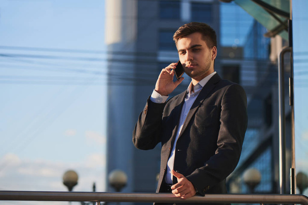 young businessman in suit talking on phone while standing on porch of business building - Zdjęcie, obraz
