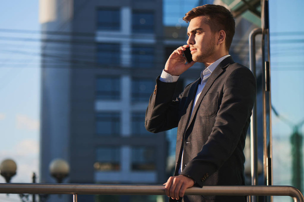 young businessman in suit talking on phone while standing on porch of business building - Foto, immagini