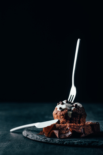 Delicious muffin with glaze and silverware set on dark background - Fotoğraf, Görsel