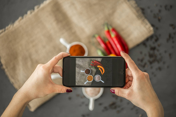 Top view of a blogger taking a photo of spices in stylish ceramic dishes for her culinary blog with a smartphone - Valokuva, kuva