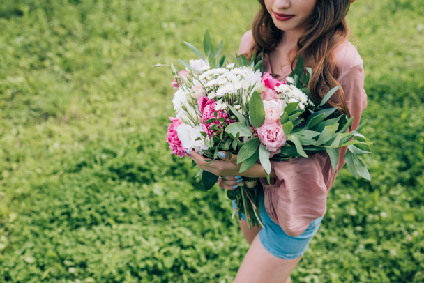 公園内の花の花束を持つ若い女性の部分的なビュー手します。 - 写真・画像