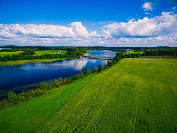 Vista aérea na ponte sobre o lago azul no dia de verão no campo rural da Finlândia com campos verdes e amarelos
 - Foto, Imagem