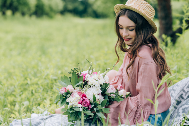 vue latérale de belle femme souriante avec bouquet de fleurs reposant sur une couverture dans le parc
 - Photo, image