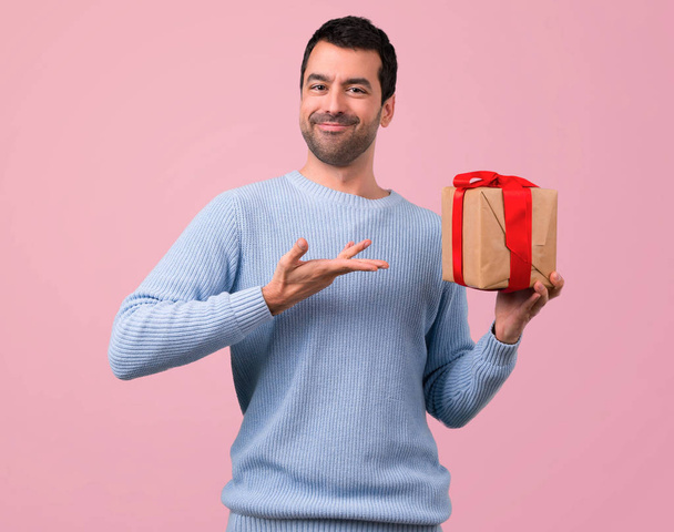 Man with blue sweater holding gift boxes in hands on pink background - Фото, изображение