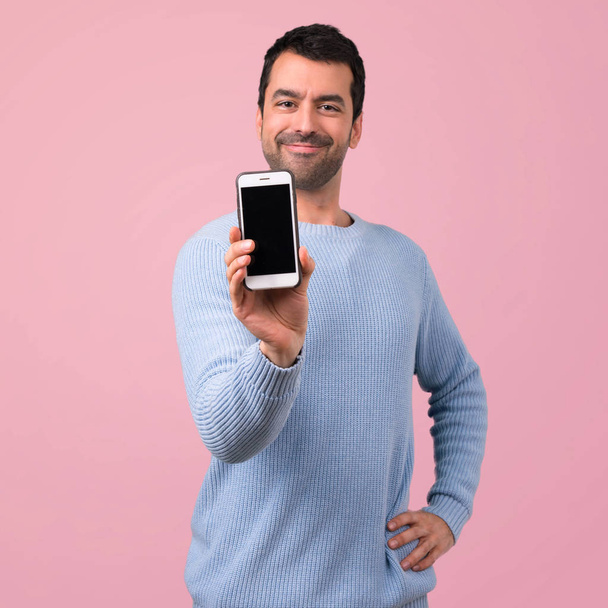 Mann mit blauem Pullover mit Handy auf rosa Hintergrund - Foto, Bild