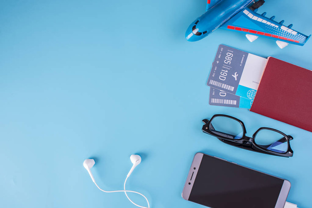 Αεροπλάνο, Αεροπορικά Εισιτήρια, διαβατήριο, γυαλιά και τηλέφωνο με ακουστικά σε μπλε φόντο. Η θέα από την κορυφή. Η έννοια του προγραμματισμό και την προετοιμασία για το ταξίδι - Φωτογραφία, εικόνα