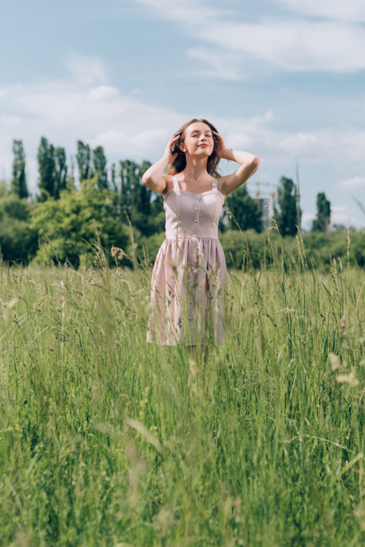 portrait of young beautiful woman in stylish dress standing in meadow alone - 写真・画像