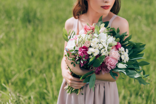 partial view of woman holding bouquet of flowers while standing in field alone - Φωτογραφία, εικόνα