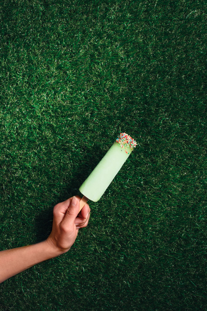 Delicious popsicle in hand on green grass background - Photo, Image