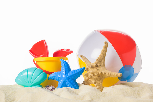 Strandbal en speelgoed in zand geïsoleerd op wit - Foto, afbeelding